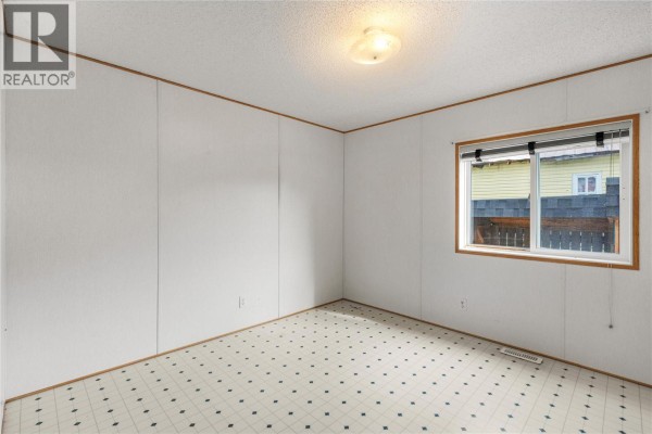 Empty room with white panel walls, patterned linoleum floor, and a single window. - 5694 97 Highway, Falkland