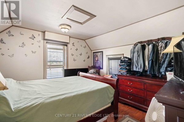 A bedroom with a green-covered bed, dark wood dresser, and butterfly decals on the wall. - 5694 Duncan Street, South Dundas