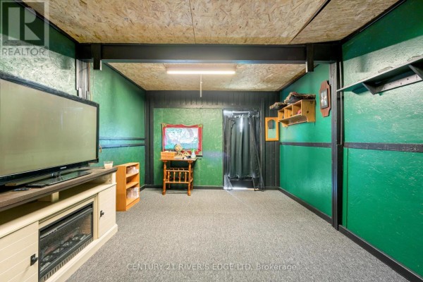 A room with green walls, grey carpet, a television, and a wooden side table. - 5694 Duncan Street, South Dundas
