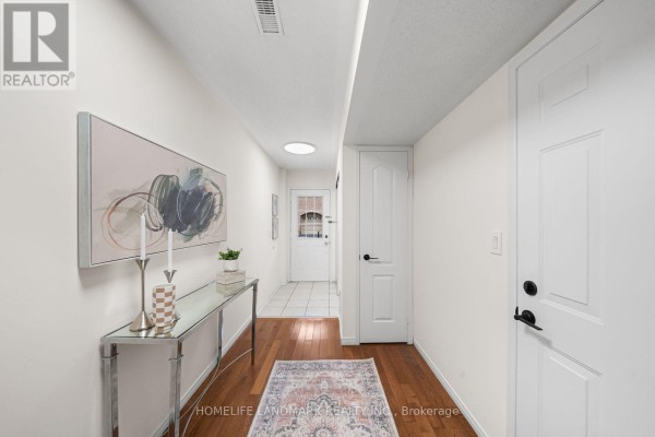 Interior hallway with hardwood floors, white walls, artwork, console table, and a tiled entryway. - 57 - 3 Brisby Mews, Toronto