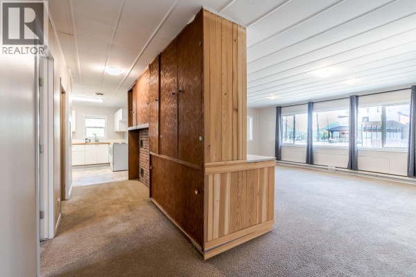 White kitchen with wood-look flooring, white cabinets, and stainless steel appliances. - 57 12th Avenue, Lillooet