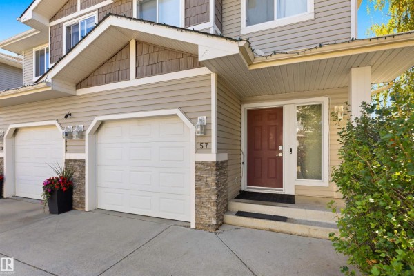 Close-up of duplex entrance with burgundy door, stone accents, and two garage doors. - #57 133 Eastgate Wy, St  Albert