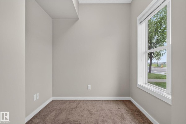 Empty room with beige carpet, neutral walls, and a window overlooking a street. - #57 3710 Allan Dr Sw, Edmonton