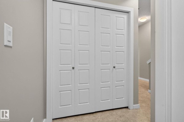 White bi-fold closet doors in a hallway with beige carpet and a ceiling light. - #57 3710 Allan Dr Sw, Edmonton