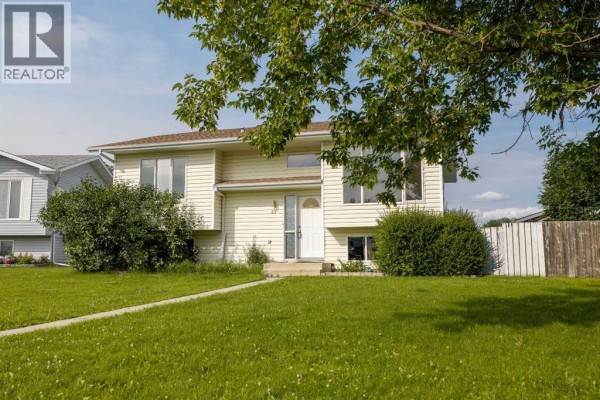 Front facade of a pale yellow house with a white front door and green landscaping. - 57 Atkinson Crescent, Whitecourt