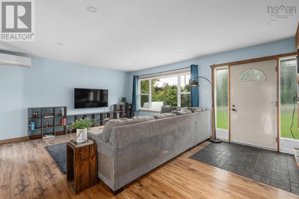 Living room with light blue walls, a grey sectional sofa, wood flooring, and a large window facing the yard. - 57 Bayview Drive, Whites Lake