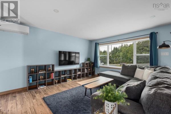 Living room with light blue walls, grey sectional sofa, dark blue rug, entertainment unit, and large window with green trees outside. - 57 Bayview Drive, Whites Lake