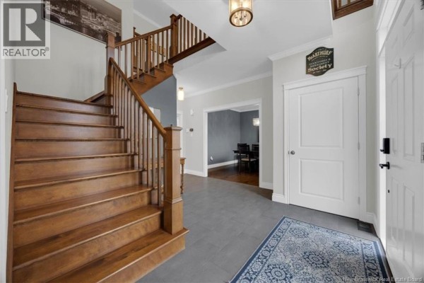 Wide view of wooden staircase and entryway with gray tiled floor, white doors, and dining room entrance. - 57 Colchester Drive, Quispamsis