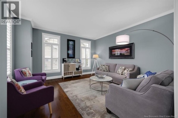 Living room with blue walls, gray sofas, purple accent chairs, white shutters, and a large area rug. - 57 Colchester Drive, Quispamsis