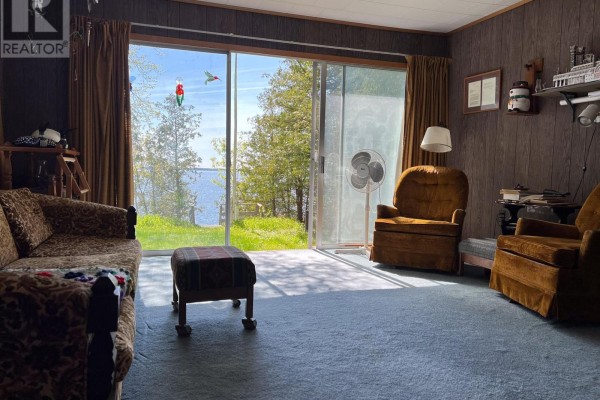 A living room with a sofa, chairs, and sliding glass doors offering a view of trees and water. - 57 Island View Road, Kawartha Lakes