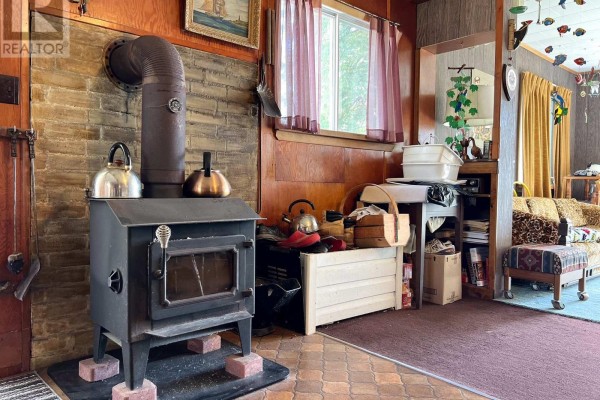 A wood-burning stove with kettles on top, next to a brick hearth and paneled walls. - 57 Island View Road, Kawartha Lakes