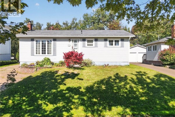 Side exterior view of a single-story home with white vinyl siding, green lawn, and attached garage. - 57 Labrosse Road, Moncton
