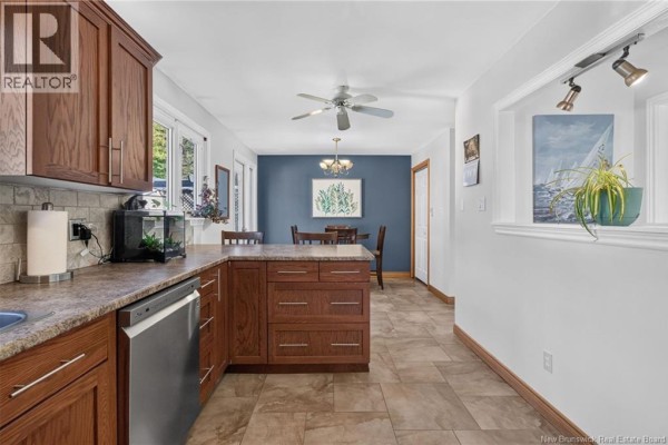 Kitchen with oak cabinets and stainless steel appliances, open to a dining area with blue walls. - 57 Labrosse Road, Moncton