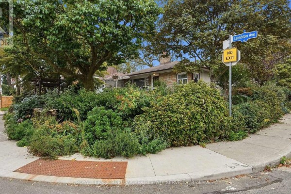 Corner view of the property showcasing dense foliage and street signage. - 57 Lambton Avenue, Toronto