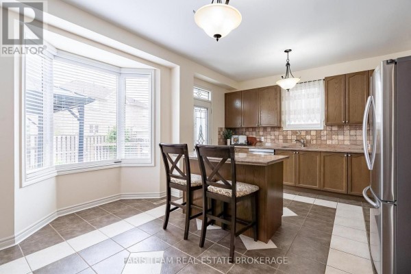 Kitchen with bay window, island with two stools, and wood cabinets. - 57 Spotted Owl Crescent, Brampton