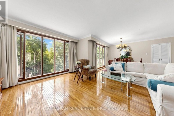 Living room with large windows overlooking trees, white sofa, armchair, and wooden floors. - 57 Sumner Heights Drive, Toronto