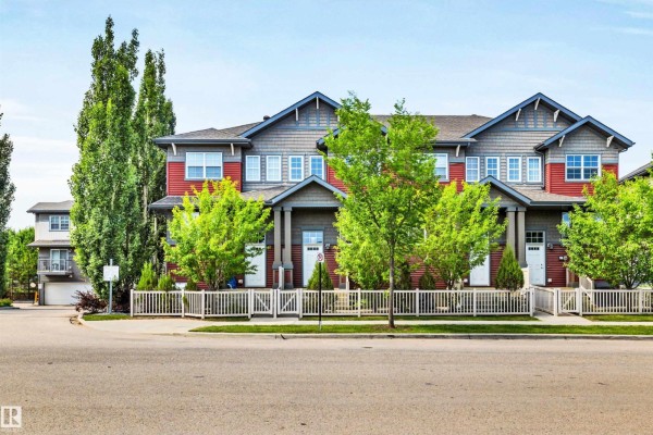 Street view of a townhouse complex with red and grey exteriors and mature trees. - 571 Orchards Bv Sw, Edmonton