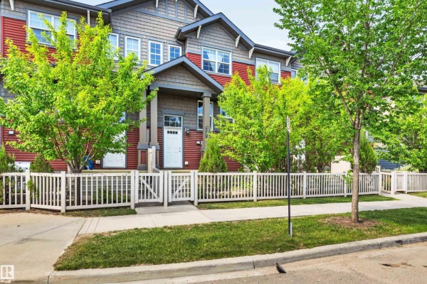 Close-up of a red townhouse unit with grey accents, a white door, and picket fence. - 571 Orchards Bv Sw, Edmonton