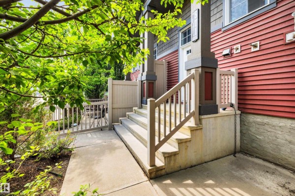 Side view of townhouse stairs and porch with a wooden railing and green foliage. - 571 Orchards Bv Sw, Edmonton