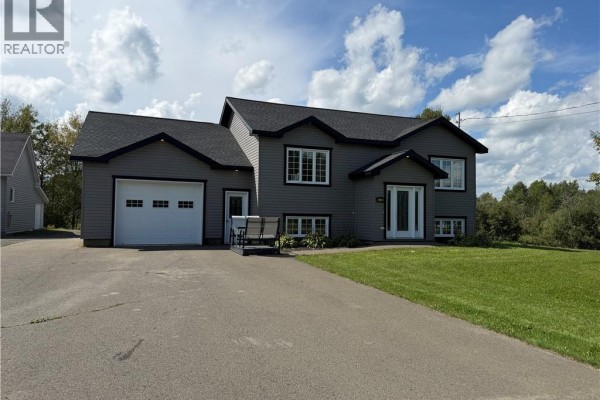 Front view of a grey residential house with white trim, windows, and a double garage door. - 5712 Route 17, Saint Quentin