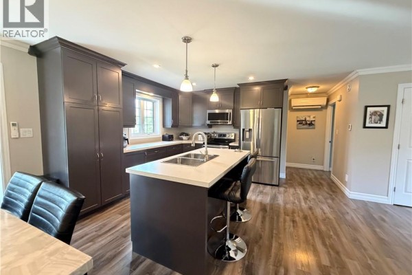 Kitchen island with a sink and bar stools, adjacent to dark grey cabinets and stainless steel refrigerator. - 5712 Route 17, Saint Quentin