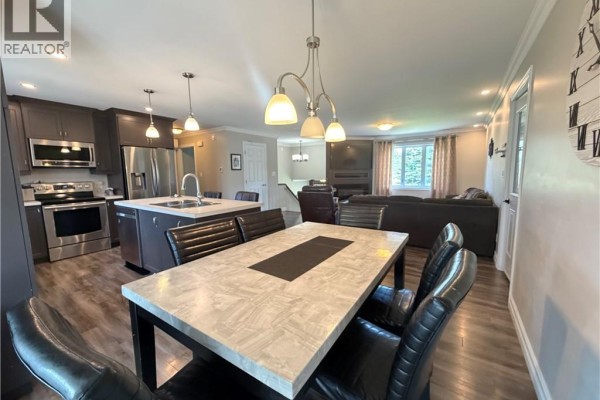 Dining table with black chairs in an open-concept kitchen and living area with a fireplace. - 5712 Route 17, Saint Quentin