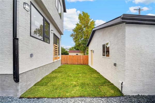 View of the side yard between the duplex and garage, featuring green grass and white stucco walls. - 572 Centennial Street, Winnipeg