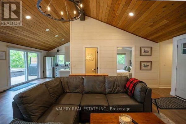 Living area with sectional sofa facing television, wood-paneled vaulted ceiling, and view into bedroom. - 572 Mallard Circle, Selwyn