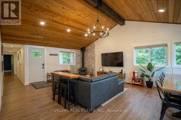 Living room showing stone accent wall, wood-burning stove, television, and dining area. - 572 Mallard Circle, Selwyn
