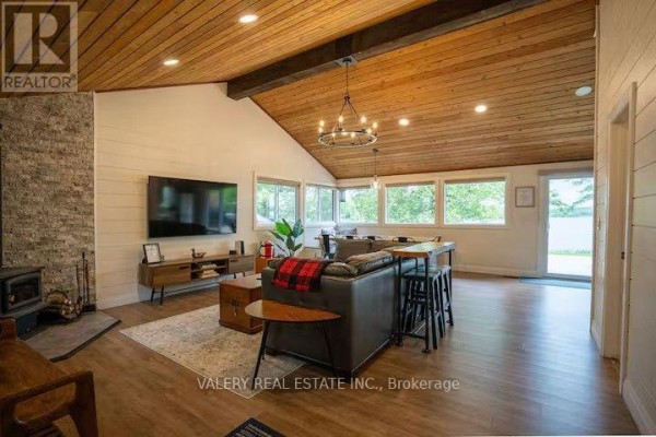 Living room with television, wood stove, and dining area visible through windows. - 572 Mallard Circle, Selwyn