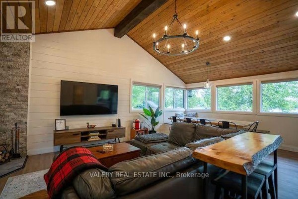Living area featuring a sectional sofa, television, wood stove, and expansive windows with nature views. - 572 Mallard Circle, Selwyn