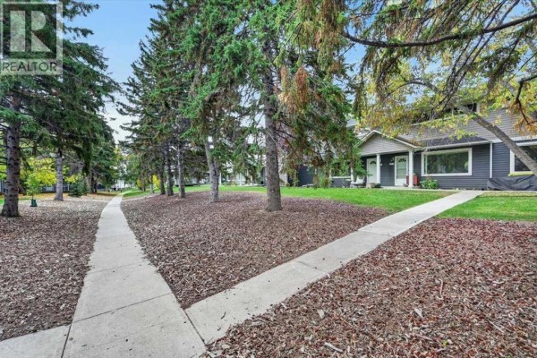 Concrete pathways diverge through a grassy area with trees and fallen leaves, leading to townhouses. - 572 Regal Park Ne, Calgary