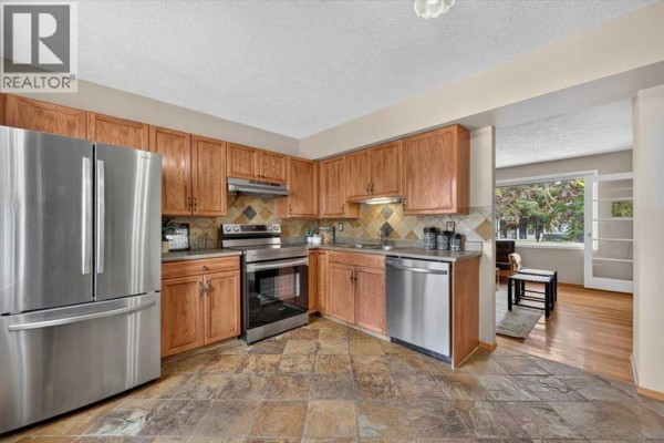 Kitchen with light wood cabinets, stainless steel appliances, and slate tile flooring, opening to a living area. - 572 Regal Park Ne, Calgary
