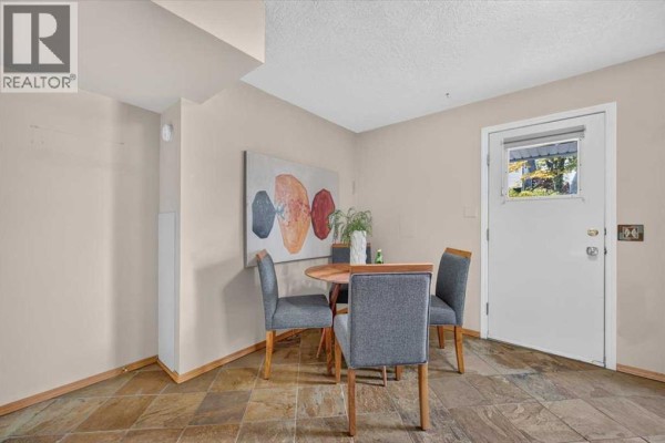 Dining nook with a round table, grey chairs, and a door leading outside; slate tile floor. - 572 Regal Park Ne, Calgary