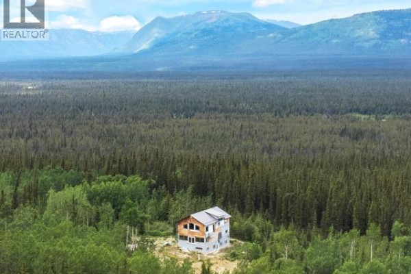 Distant aerial view of a house with unfinished construction, set against a backdrop of forest and mountains. - 572 Robinson Subdivision, Whitehorse South