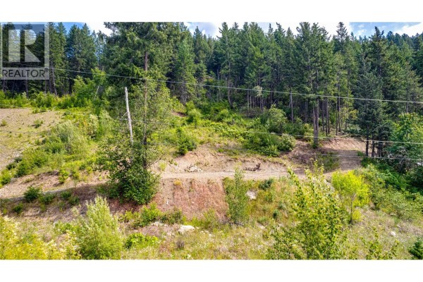 Cleared hillside lot with trees, shrubs, and visible utility poles. - 5720 Hartnell Road Unit# 7, Vernon