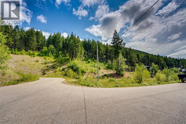 Paved road intersection with a clear lot on the right and forested hillside beyond. - 5720 Hartnell Road Unit# 7, Vernon