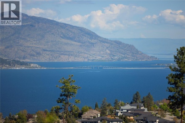 Panoramic view of a city skyline across a lake with layered mountains in the background. - 5723 Jasper Way, Kelowna