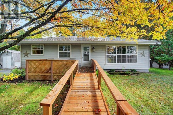 Front view of a light gray, single-story house with a metal roof, accessed by a wooden walkway and ramp. - 5724 Route 105, Mill Cove