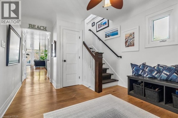 Interior hallway with wooden floors, a staircase, and a dark bench with blue cushions. - 573 Beach Boulevard, Hamilton
