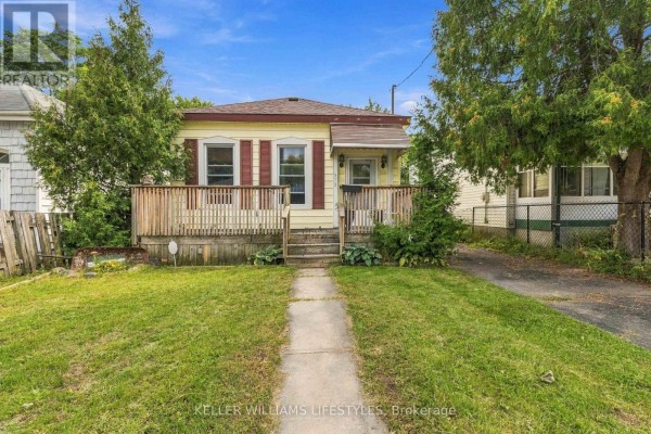 Front view of a yellow bungalow with a covered porch and wooden railings. Evergreen trees flank the lawn. - 573 Hill Street, London East