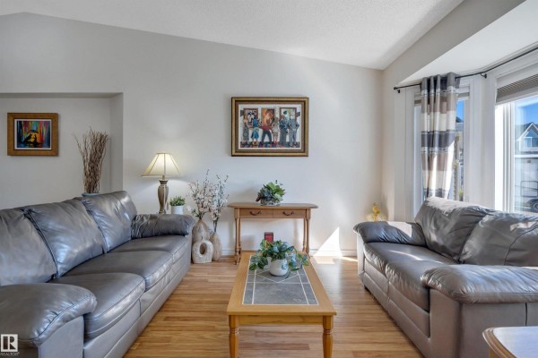 Living room furnished with a leather sofa, coffee table, console table, and large windows with striped curtains. - 5735 152a Av Nw, Edmonton