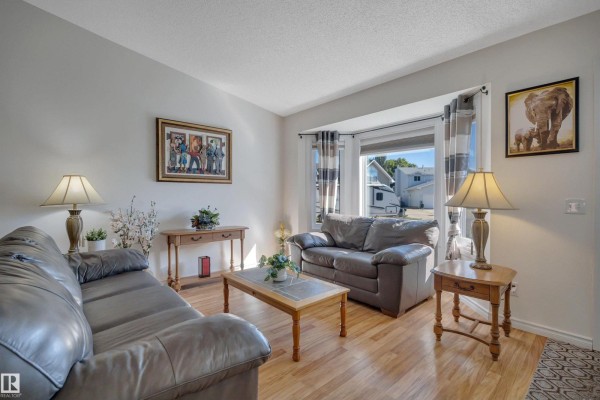 Living room featuring two sofas, a coffee table, decorative lamps, and a bay window with a view of the street. - 5735 152a Av Nw, Edmonton