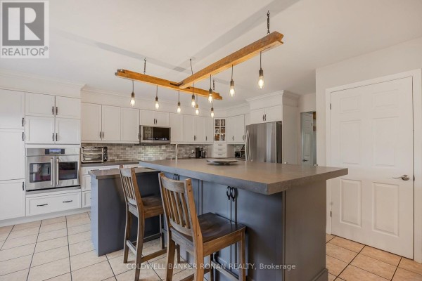 Kitchen with white cabinets, stainless steel appliances, and a grey island with two bar stools. - 5735 Concession Rd 6, Adjala Tosorontio