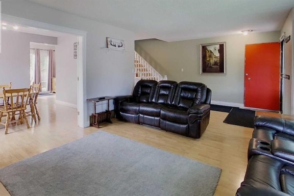 Living room with a dark leather sofa, a grey rug, and an adjacent dining area. - 5735 Westhaven Drive, Edson