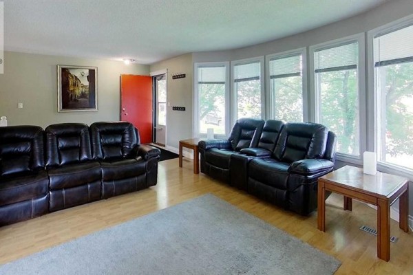 Living room with bay windows, dark leather sofas, wood side tables, and a grey rug. - 5735 Westhaven Drive, Edson