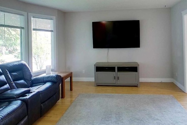 Living room with a large television mounted on the wall above a grey media console. - 5735 Westhaven Drive, Edson