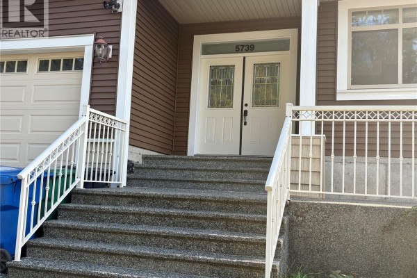 Front entrance of a brown house with double white doors and a set of stone stairs. - 5739 Bradbury Rd, Nanaimo