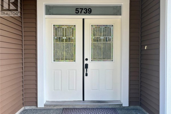 Close-up of the double white front doors with decorative glass panels and the house number 5739. - 5739 Bradbury Rd, Nanaimo