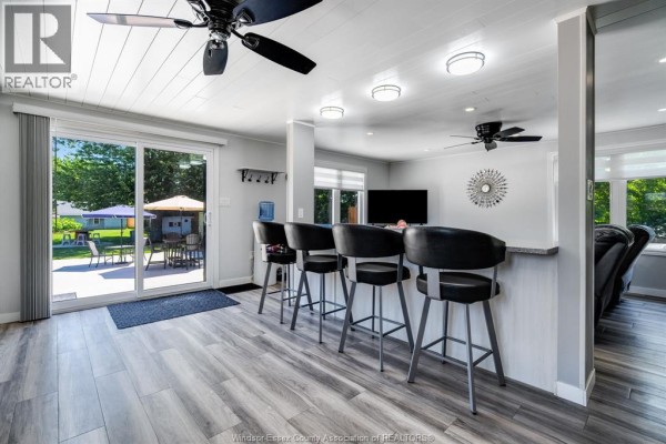 Interior view of a kitchen island with bar stools, a television, and sliding doors to the backyard. - 574 Bevel Line, Leamington